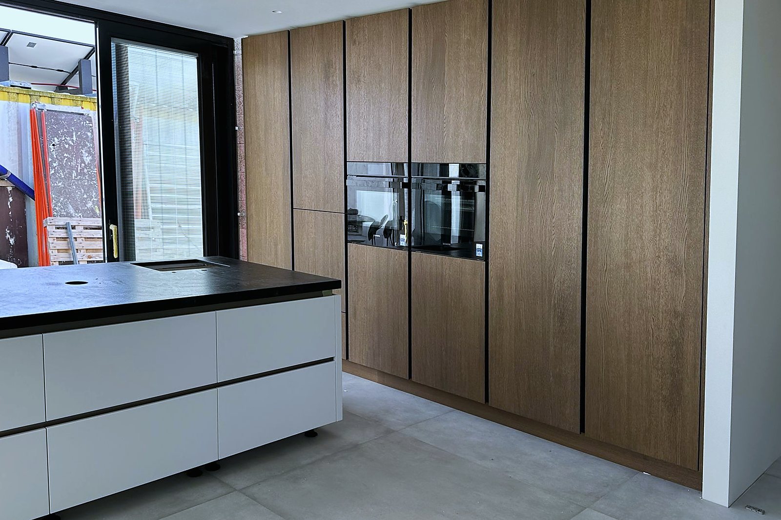 Walnoot kastenwand met inbouwapparatuur tegenover een wit kookeiland met donker werkblad, door Maatmakers Interieurbouw