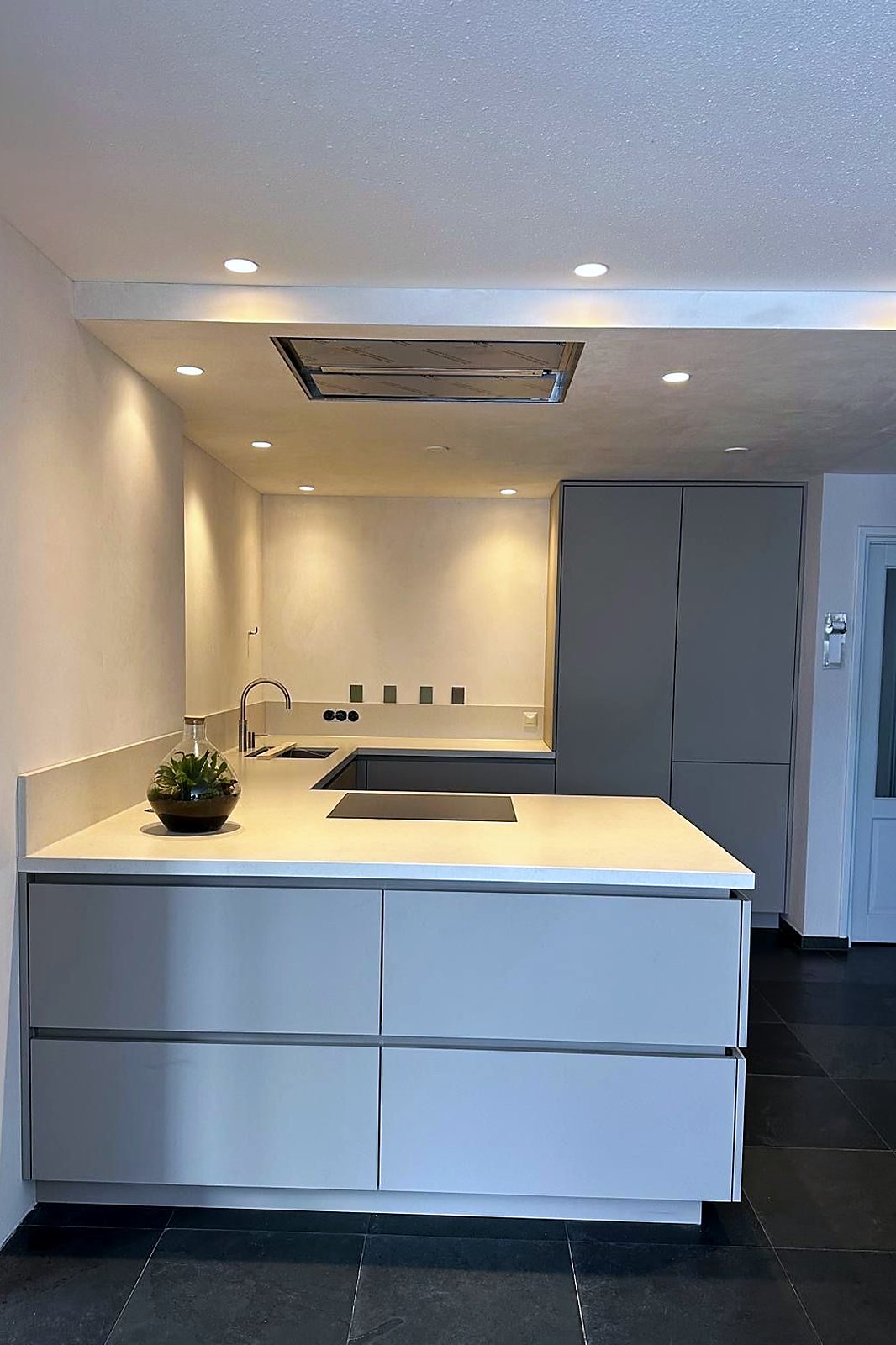 Zijaanzicht van de grijze greeploze keuken met kookplaat in het werkblad, door Maatmakers Interieurbouw
