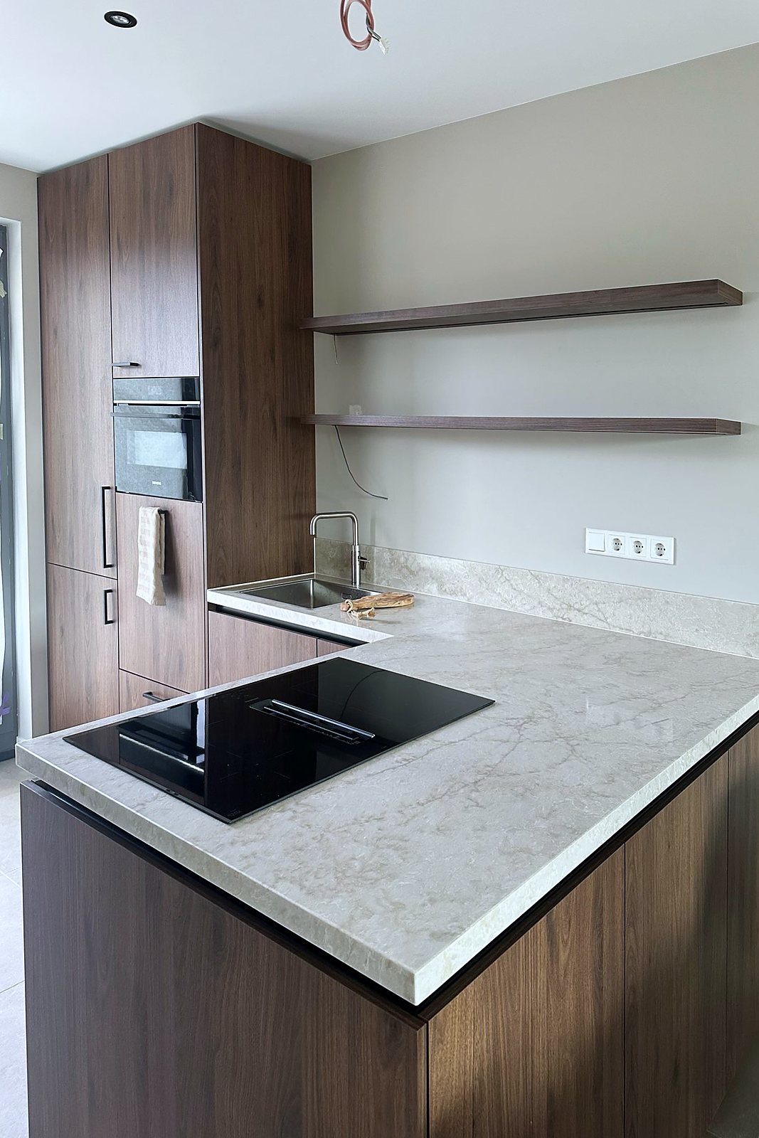 Detail van de walnoot keuken met kookplaat in het lichte natuursteenblad, door Maatmakers Interieurbouw