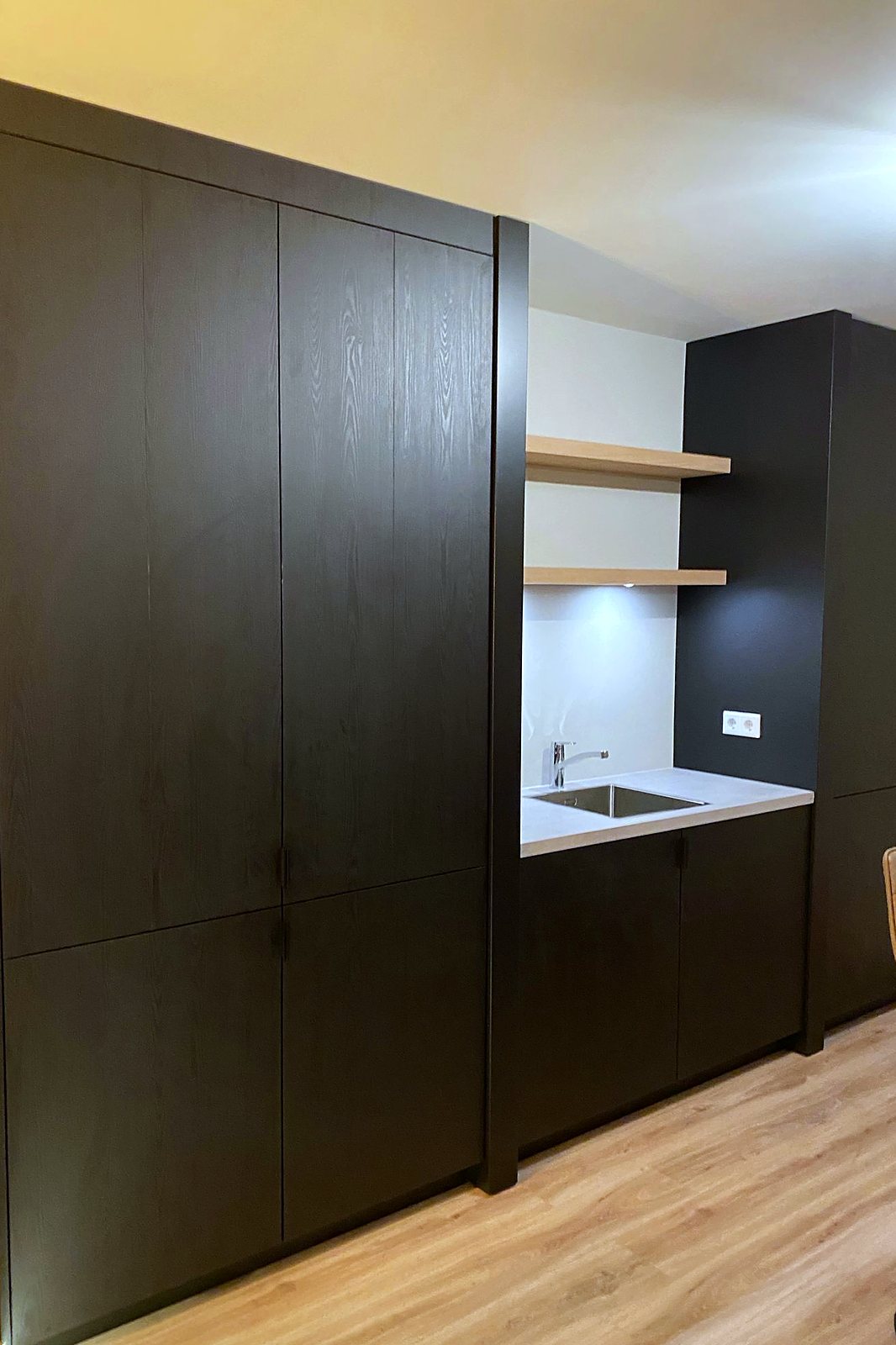 Vlakke kastenwand in donker eiken tot aan het plafond met verdiept spoelgedeelte en open planken, door Maatmakers Interieurbouw
