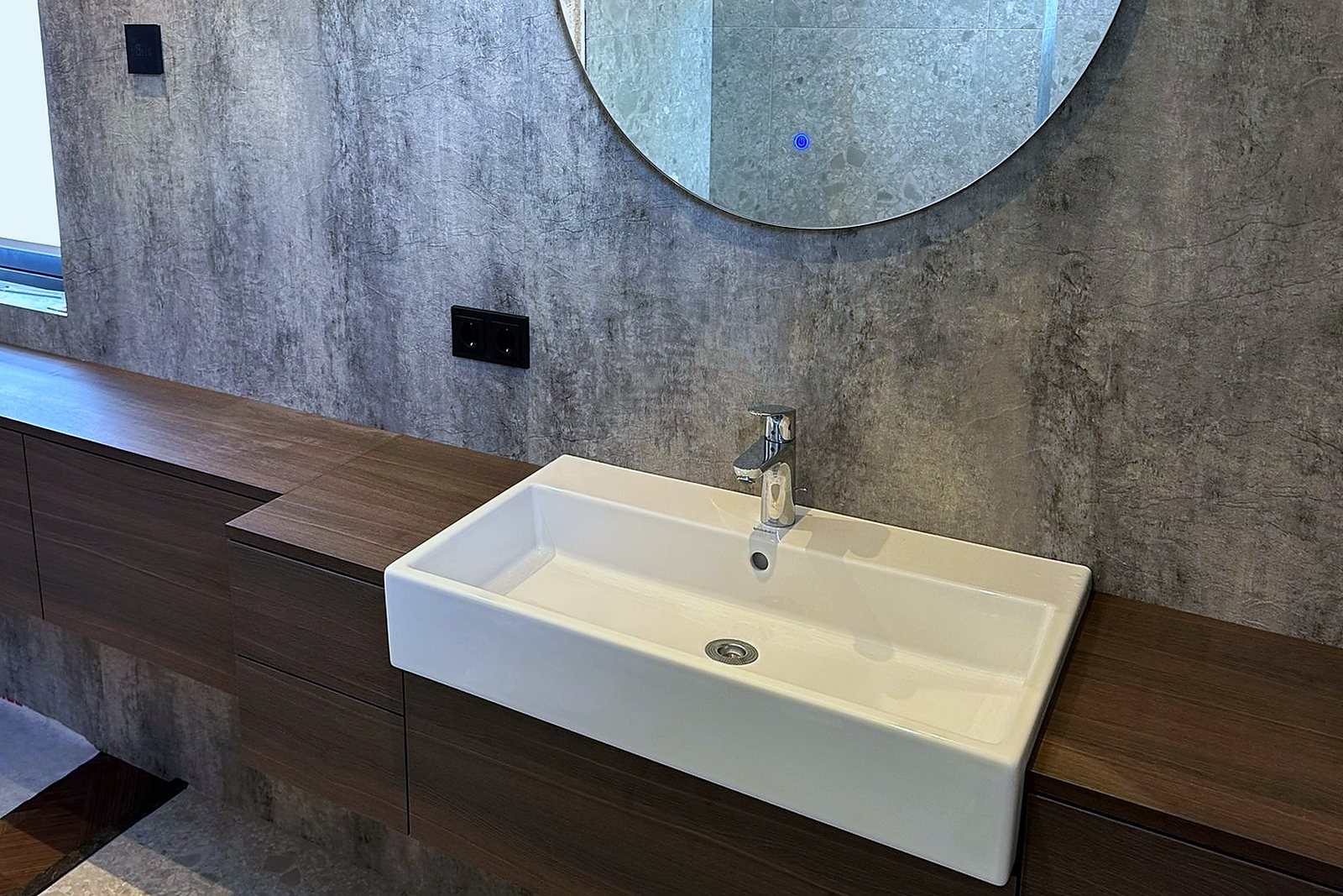 Zwevend walnoot badkamerblad met witte opzetkom tegen een betonlook wand met ronde spiegel, door Maatmakers Interieurbouw