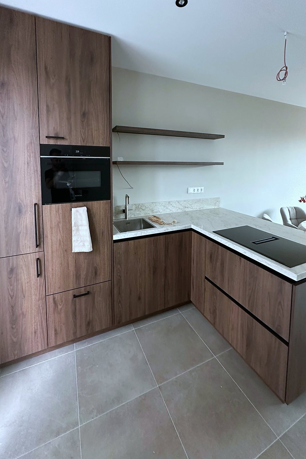 Walnoot keuken in hoekopstelling met licht natuursteenblad en zwevende planken, door Maatmakers Interieurbouw