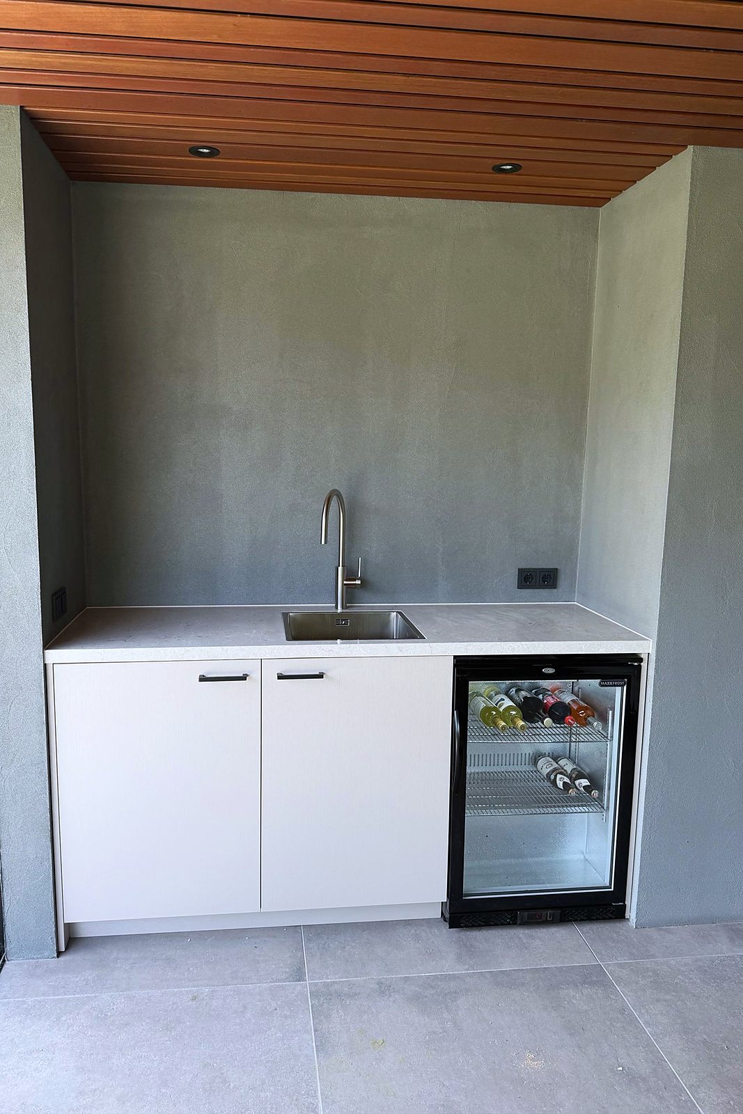 Witte kitchenette met spoelbak en ingebouwde wijnkoeler met glazen deur in een betonlook-nis, door Maatmakers Interieurbouw