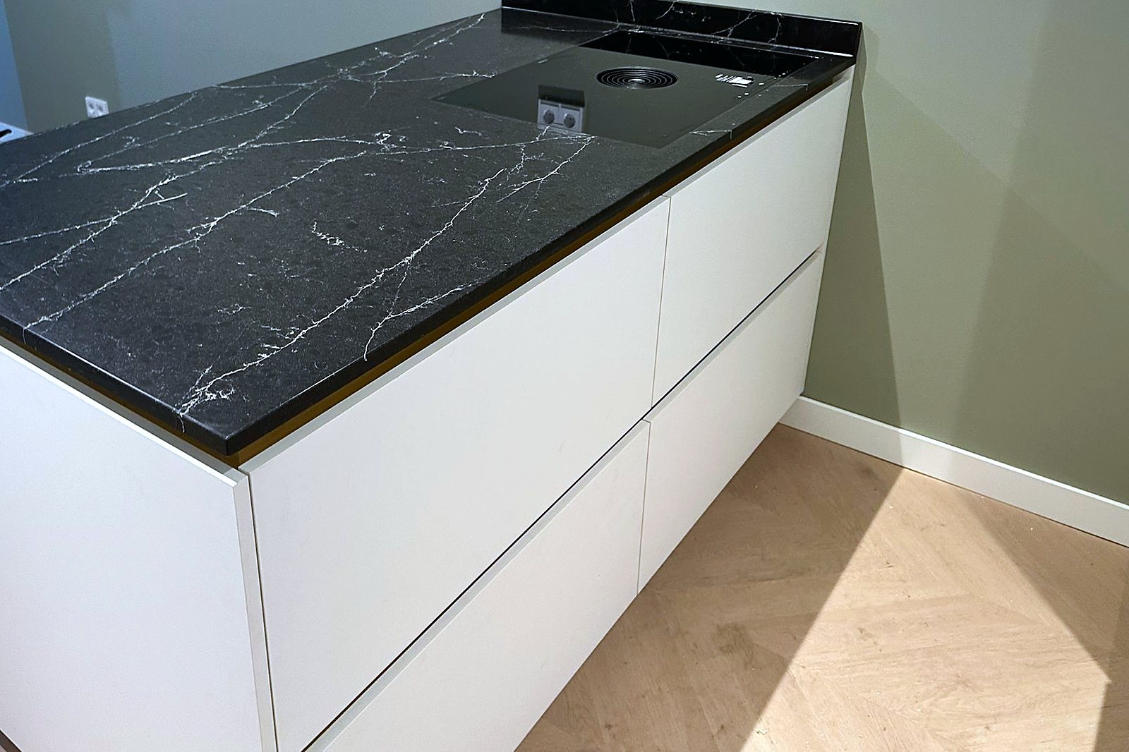 Wit greeploos kookeiland met zwart marmerlook blad en messing kraan, door Maatmakers Interieurbouw