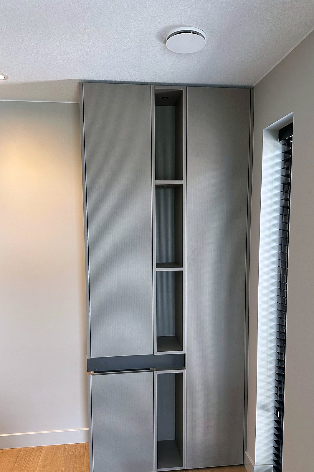 Grijze kledingkast met ribbelfront en open vakken met hanggedeelte, ingepast tussen wand en doorgang, door Maatmakers Interieurbouw