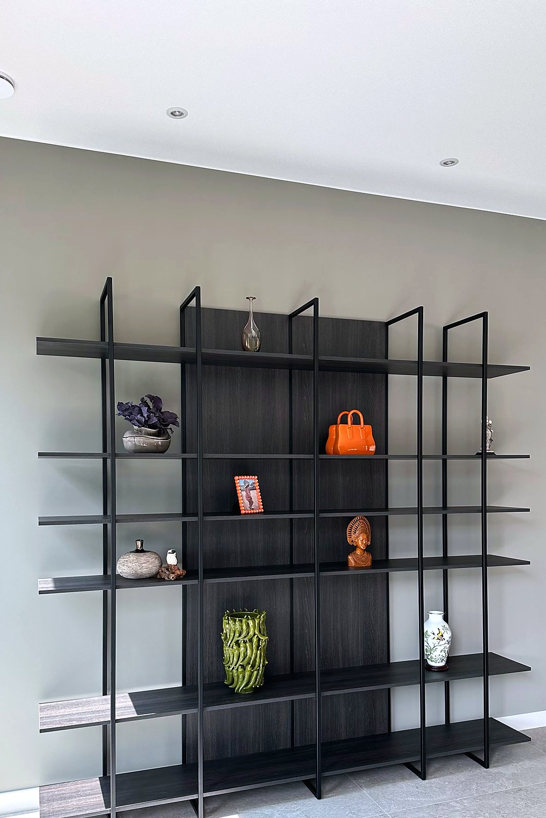 Open wandkast met slank stalen frame en donkere houten legplanken tegen een lichte wand, door Maatmakers Interieurbouw